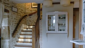 Una escalera con paredes de piedra y escalones de madera que conduce a una habitación con un armario blanco que contiene varios platos.