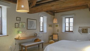 Un dormitorio con una cama de madera, un banco, una silla, un estante con fotografías y una lámpara colgante.