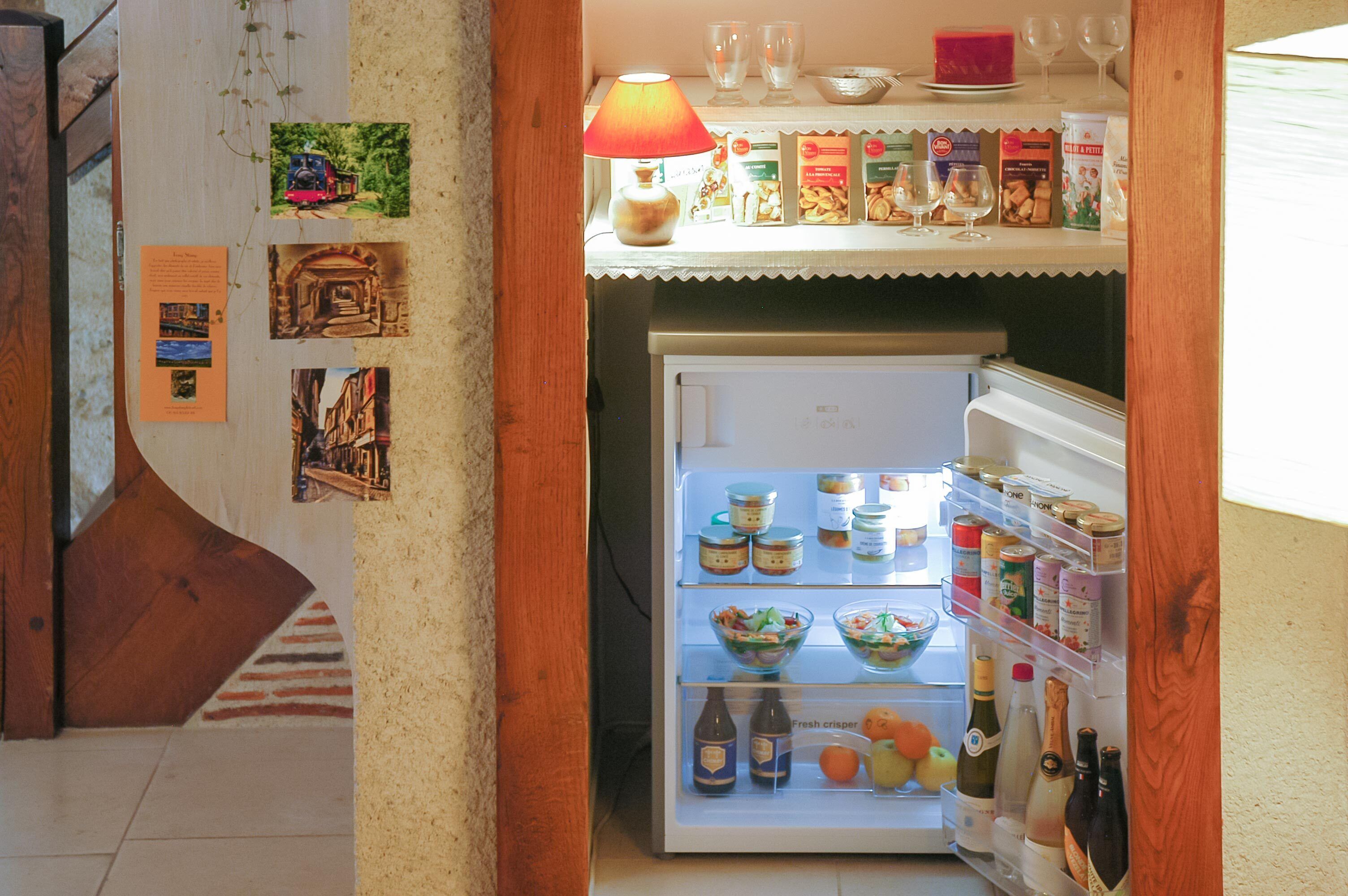 Eine Küche mit Kühlschrank, der mit Lebensmitteln und Getränken gefüllt ist, einer Holztür und einer Wand mit Bildern.