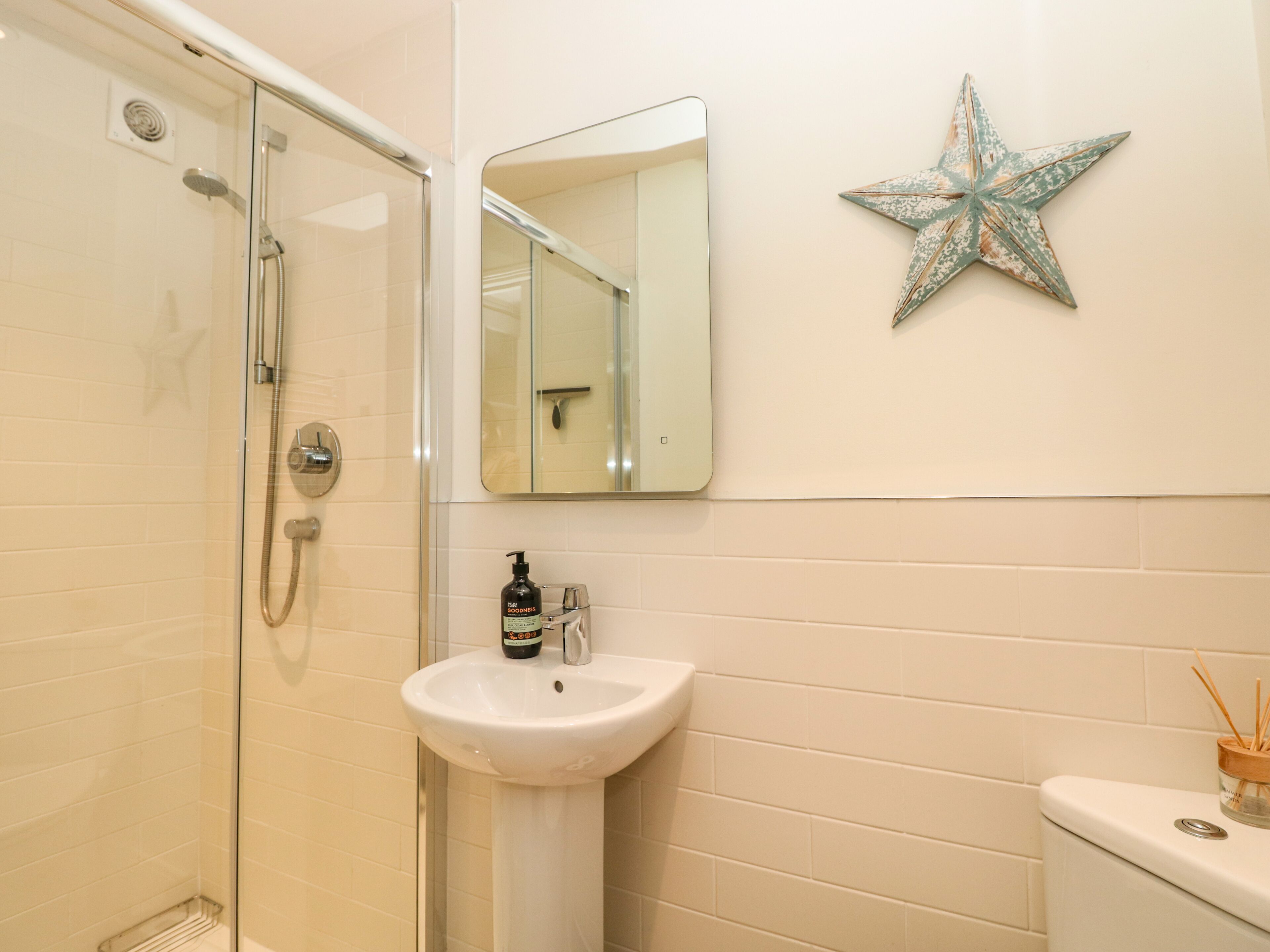A bathroom with a glass shower enclosure, a white sink, a mirror, and a decorative star on the wall.