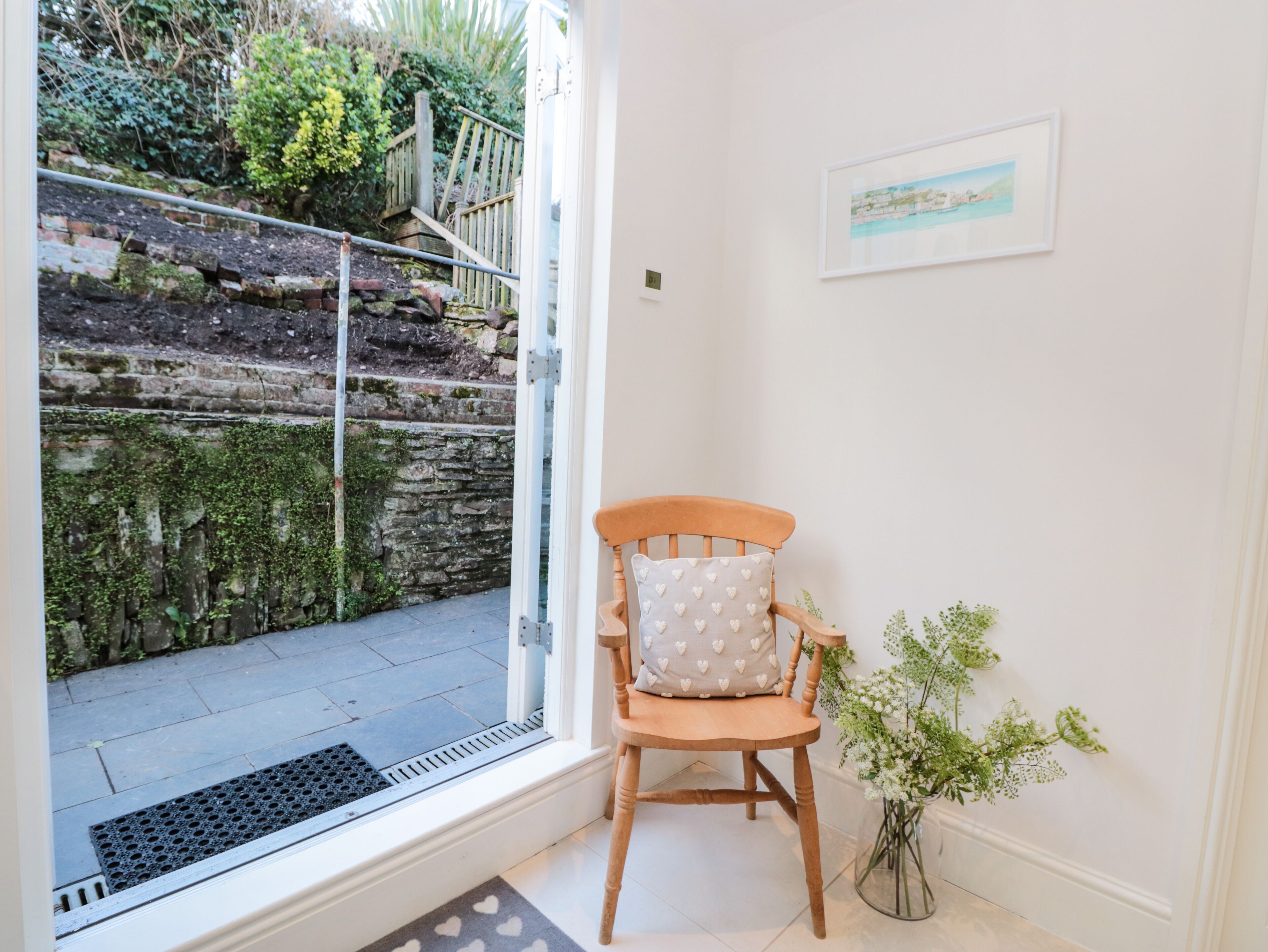 A corner of a room with a wooden chair, a small potted plant, and a framed picture on the wall.