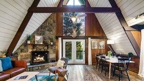 A cozy, rustic interior with a stone fireplace, wooden beams, and a dining area with a table and chairs.