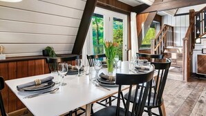 A dining area with a white table set for six, surrounded by black chairs. A vase with green foliage is on the table.
