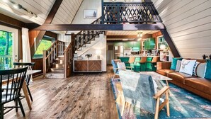A spacious loft with a wooden floor, a staircase, a dining area, and a living room with a sofa and chairs.