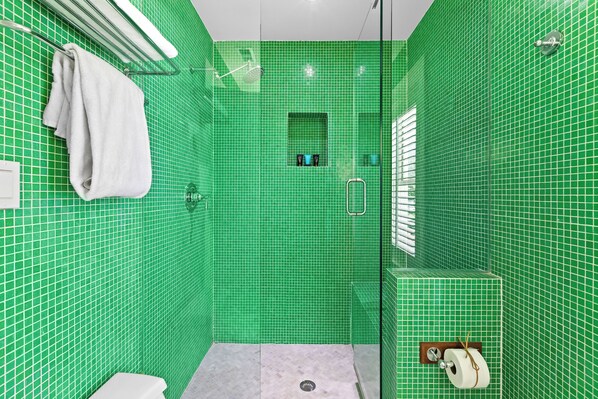 A bathroom with green tiled walls, a white towel hanging on a rack, a shower area, and a toilet with a paper towel holder. - Renovated Stunner 2 Minutes to Beach. Next to Heated Pool. Gulf Views and Bikes. (Santa Rosa Beach)