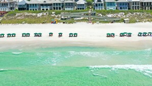 Una playa con hileras de sombrillas y una fila de casas al fondo.