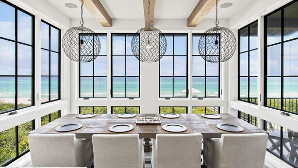 Comedor con una mesa grande dispuesta para seis personas, ventanas amplias con vistas al océano y lámparas esféricas colgantes.