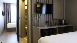 A hotel room with a bed, a TV mounted on the wall, a bedside table with a vase of flowers, and a built-in microwave. - Dilens Bosphorus Hotel (Istanbul)