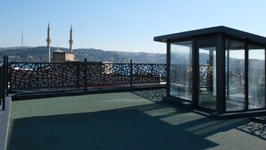 A rooftop terrace with a glass enclosure, a patterned fence, and a view of a cityscape including a tower. - Dilens Bosphorus Hotel (Istanbul)