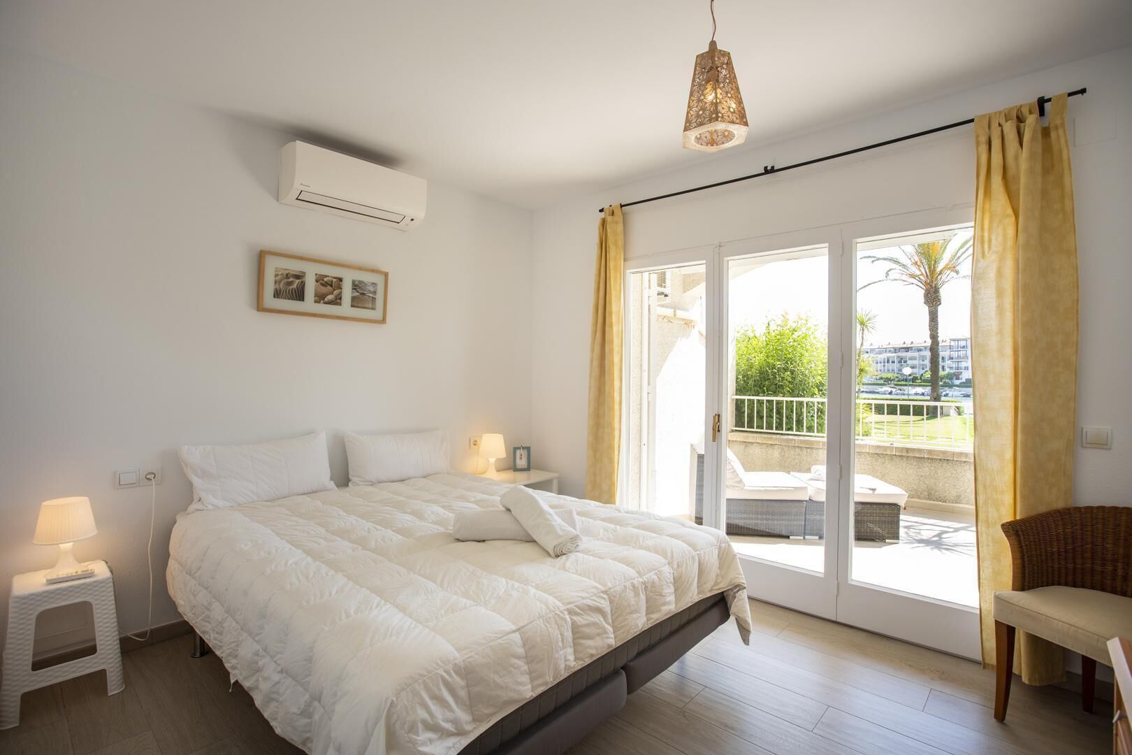 Ein Schlafzimmer mit einem Bett, Nachttischlampen, einem Bild an der Wand und Blick auf den Balkon.