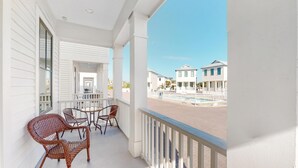 Ein Balkon mit Korbstühlen und einem Tisch, mit Blick auf einen Swimmingpool und angrenzende Gebäude.