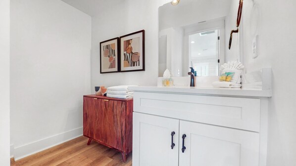 Un baño moderno con un tocador blanco, un mueble de madera y dos cuadros en la pared.