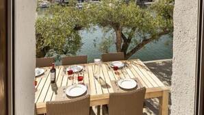 Une table en bois, dressée pour le dîner, avec vue sur une marina et les bâtiments situés de l’autre côté de l’eau.
