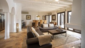 Ein geräumiges Wohnzimmer mit einer großen Couch, einem Couchtisch und einem Kamin. An der Wand befinden sich gerahmte Bilder und ein großes Fenster, das für natürliches Licht sorgt.