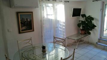 Un coin repas avec une table et des chaises en verre, une plante en pot, un tableau au mur et un ventilateur de plafond.