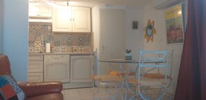 Una cocina compacta con armarios blancos, un salpicadero de azulejos y un comedor con una silla y una mesa de metal.