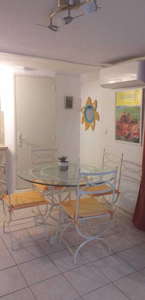 Un comedor con una mesa de vidrio y sillas de metal, un ventilador de techo, una puerta y un cartel en la pared.