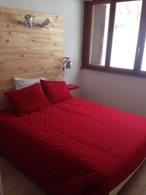 Una cama con ropa de cama roja, un cabecero de madera y una mesita de noche con una lámpara.