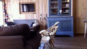 A cozy living room with a brown sofa, a blue cabinet with glass doors, and a television mounted on the wall. - La Clusaz in a quiet location 300m from the village center (La Clusaz)