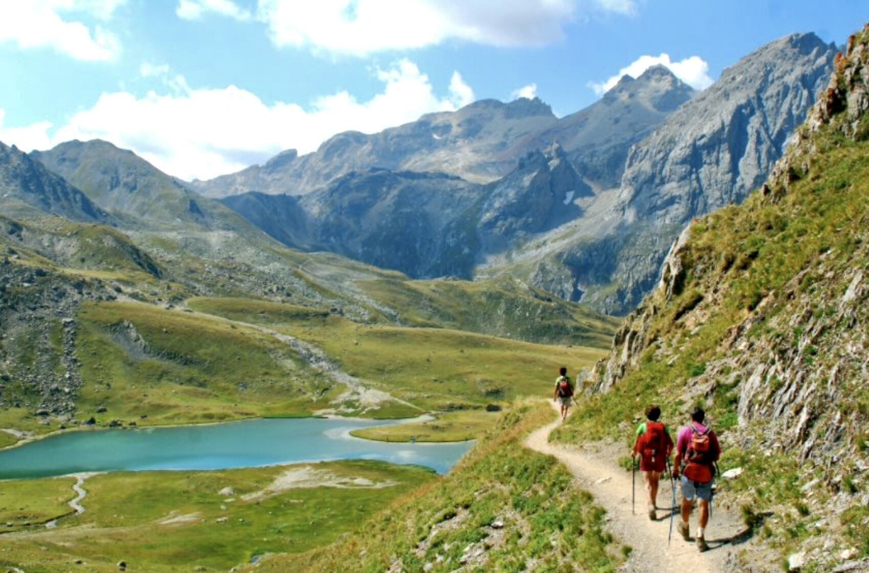 Un paysage montagneux avec un ciel dégagé, un lac et des randonneurs sur un sentier.