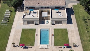 Un edificio de dos plantas con piscina, zona de estar al aire libre y cancha de tenis.