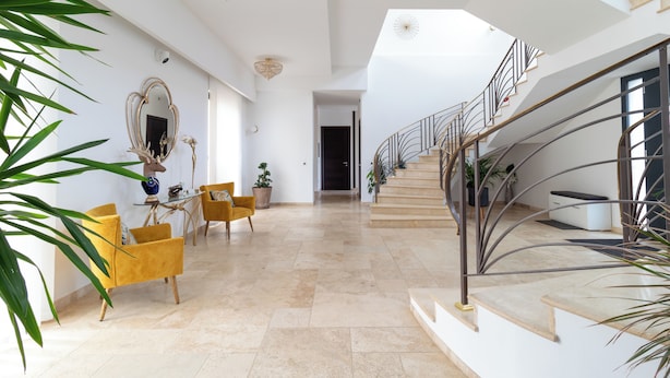 Un interior amplio con una escalera, una zona de comedor con sillas amarillas y un espejo grande.