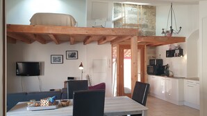En matplats med ett bord och stolar, en tv som är monterad på väggen och ett köksområde med mikrovågsugn och spis.