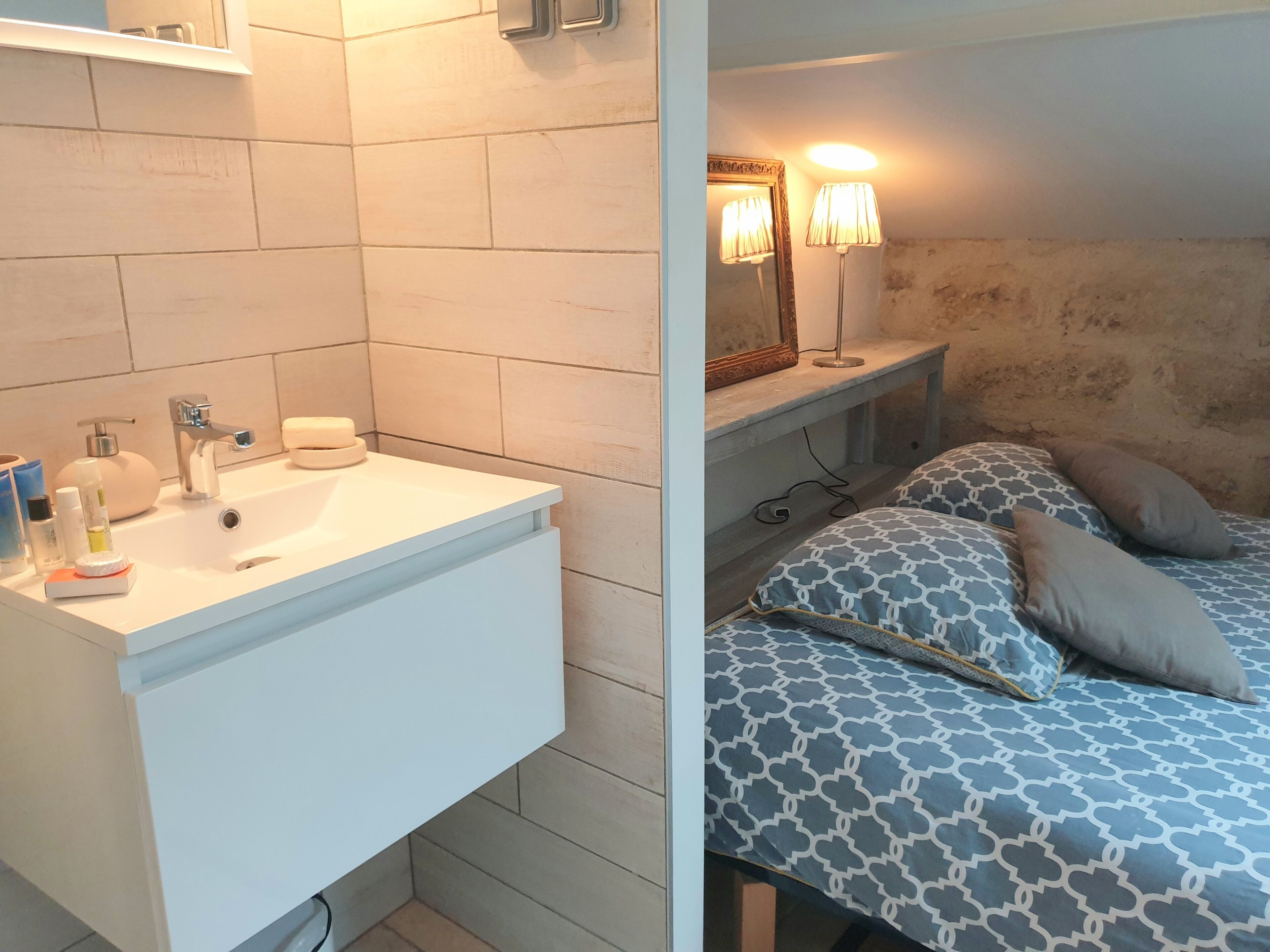 Ett badrum med ett vitt handfat, en spegel och ett sängbord med en lampa.