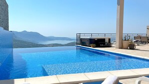 Una piscina infinita azul cristalina con vistas a montañas distantes y una masa de agua.