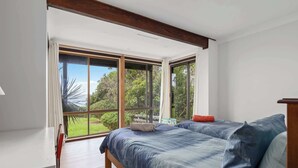 A bedroom with two beds, large windows, and a view of greenery. - Waterfront Pet-Friendly Home - Oceanview Cottage (Malua Bay)