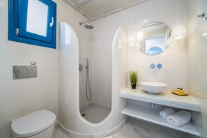 A modern bathroom with a walk-in shower, a toilet, a sink with a mirror, and a towel rack. - Kyklos luxury Villas with private pool (Santorini)