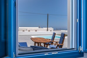 A view from a window of a room with a pool, lounge chairs, and a table. - Kyklos luxury Villas with private pool (Santorini)
