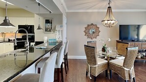 Una cocina moderna con una isla central, comedor con sillas de mimbre y una lámpara de araña.