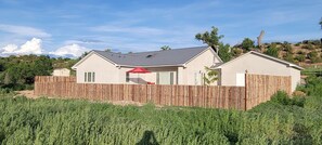 A two-story house with a fenced backyard, a red umbrella, and a view of a hilly landscape. - Casa La Capilla: Rural Creekside Retreat near SF (Santa Fe)