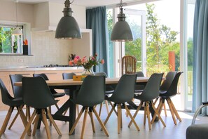 A modern kitchen with a central island, wooden chairs with wooden legs, and pendant lights.