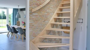 Un interior moderno con una escalera espiral de madera frente a una pared de ladrillo, que conduce a un segundo piso.