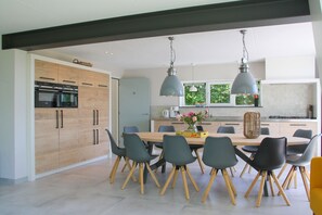 A modern kitchen with wooden cabinets, a built-in oven, and a dining area with a wooden table and chairs.
