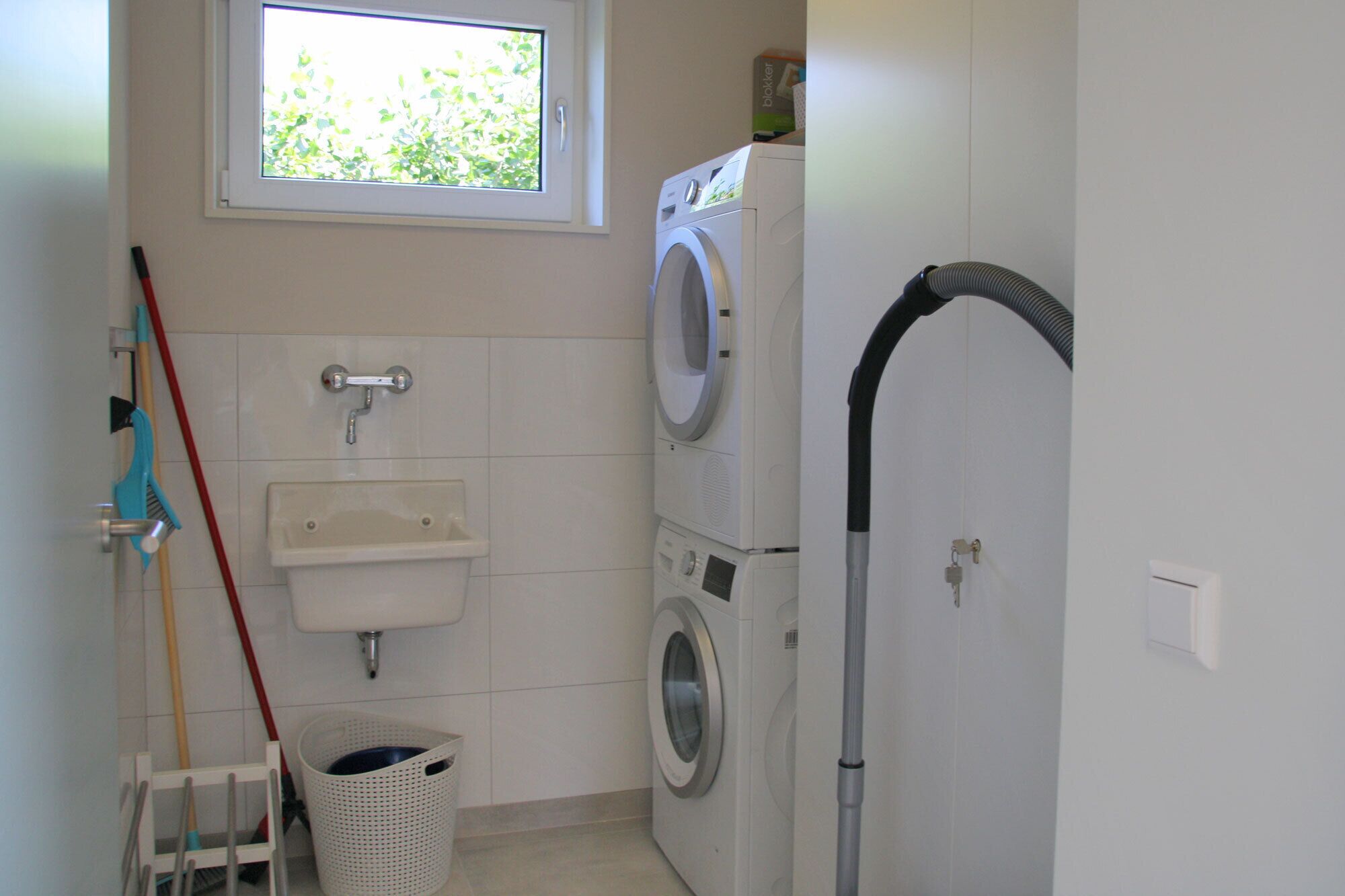 Une petite buanderie équipée d’un lave-linge, d’un sèche-linge, d’un évier et d’une fenêtre.