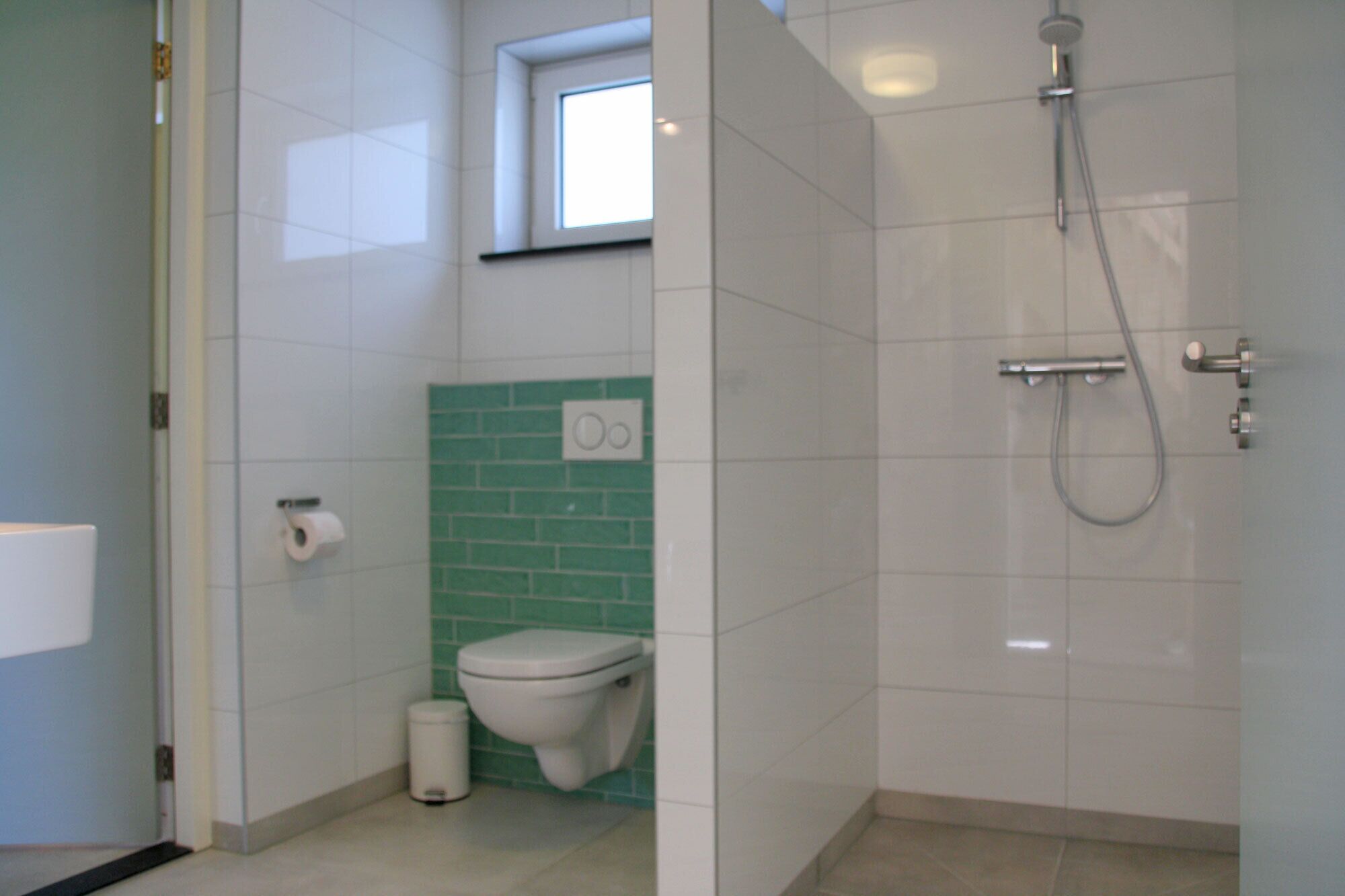 Une salle de bain équipée de toilettes, d’une poubelle, d’une douche et d’une fenêtre.