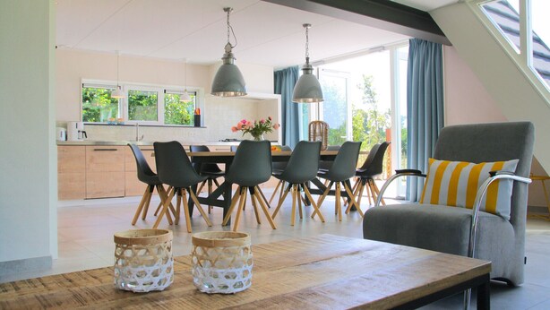 Un comedor moderno con una mesa de madera, sillas negras y lámparas colgantes.