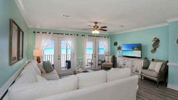 A living room with a white sofa, a television, and a view of the ocean through large windows. - Beachfront, Bayview, Relax ~ Edgewater Retreat (Cape San Blas)