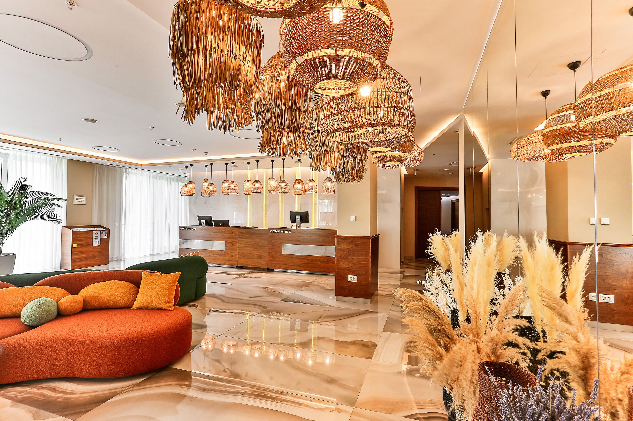 En moderne lobby med en reception, en blød orange sofa og en dekorativ hængende lampe.