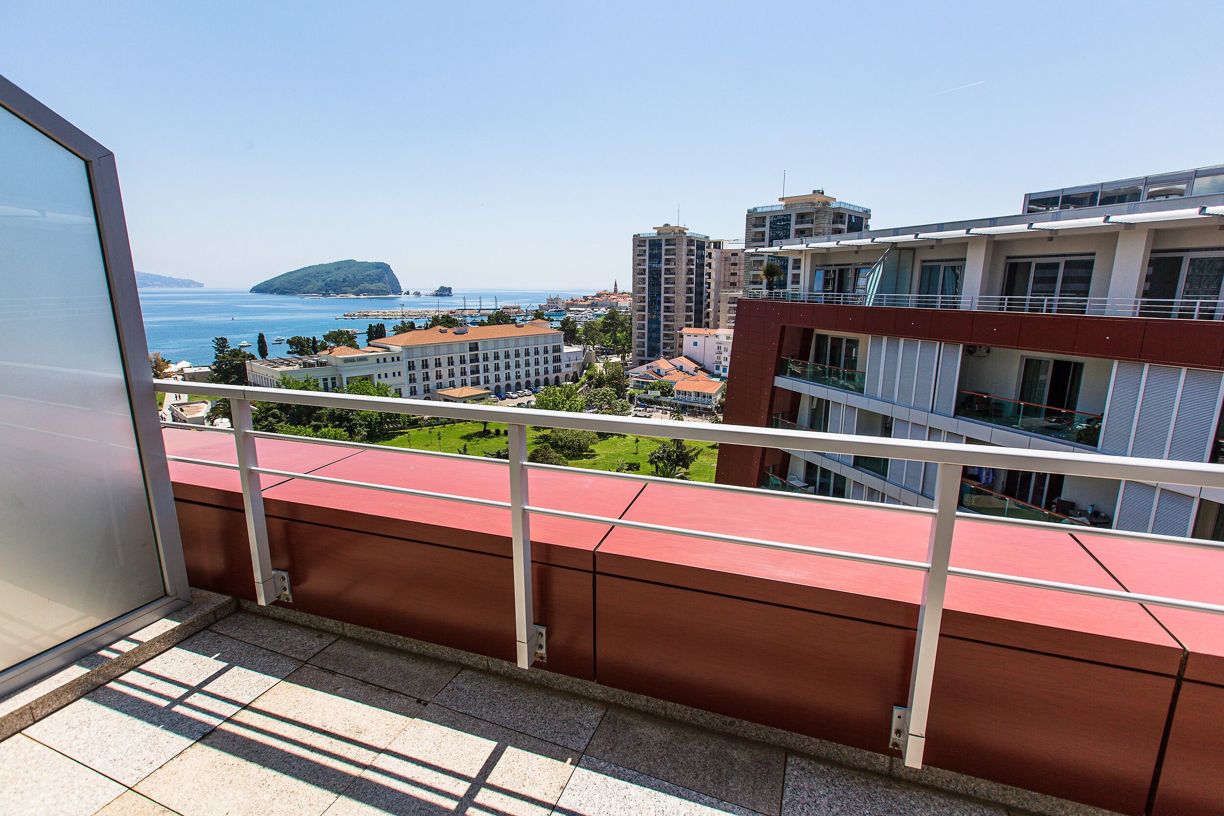 Un balcón con vistas a una ciudad costera, que incluye edificios y una isla distante.