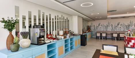 A modern hotel lobby with a light blue reception desk, a large mirror wall, and a dining area with tables and chairs.