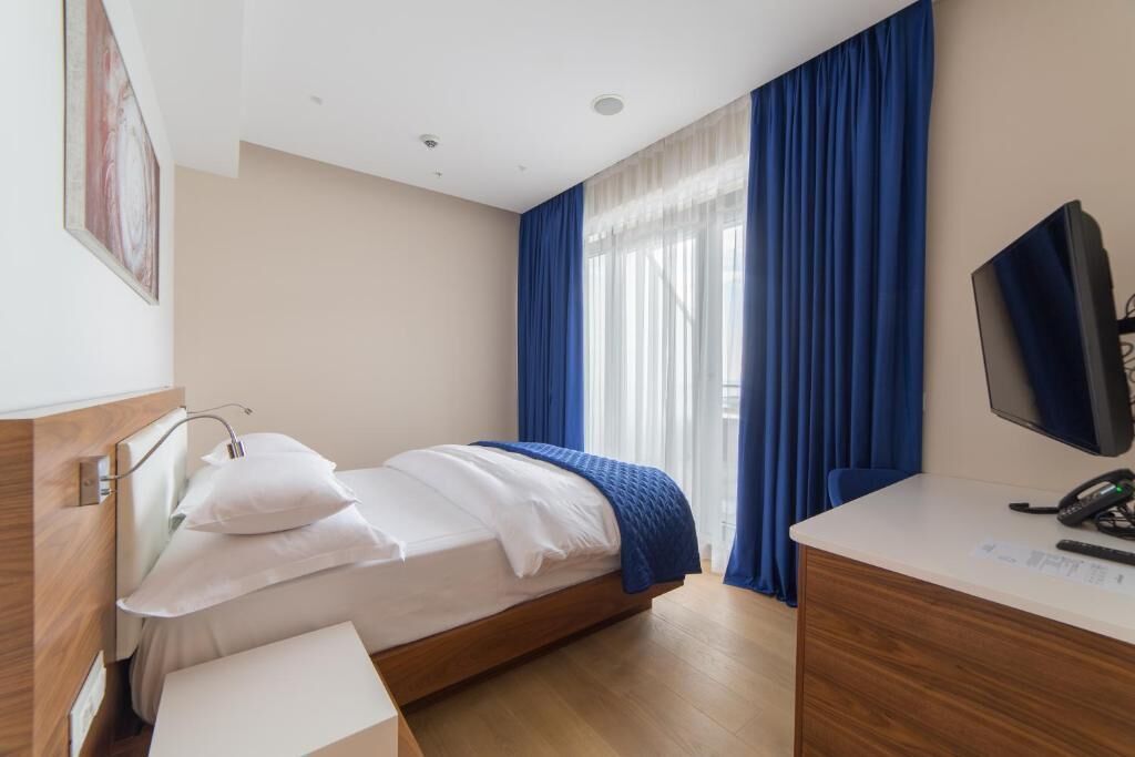 A hotel room with a bed, a desk, a television, and a window with blue curtains.