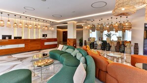 A modern lobby with a reception desk, green and orange sofas, and hanging rattan lamps. - Hotel Plaza (Budva)