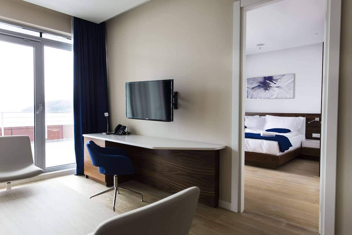 A hotel room with a desk, chair, bed, and a TV mounted on the wall.