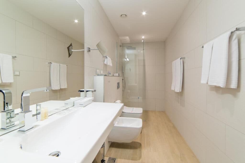 Un baño moderno con un lavamanos alargado, un inodoro y una ducha con mampara de vidrio.
