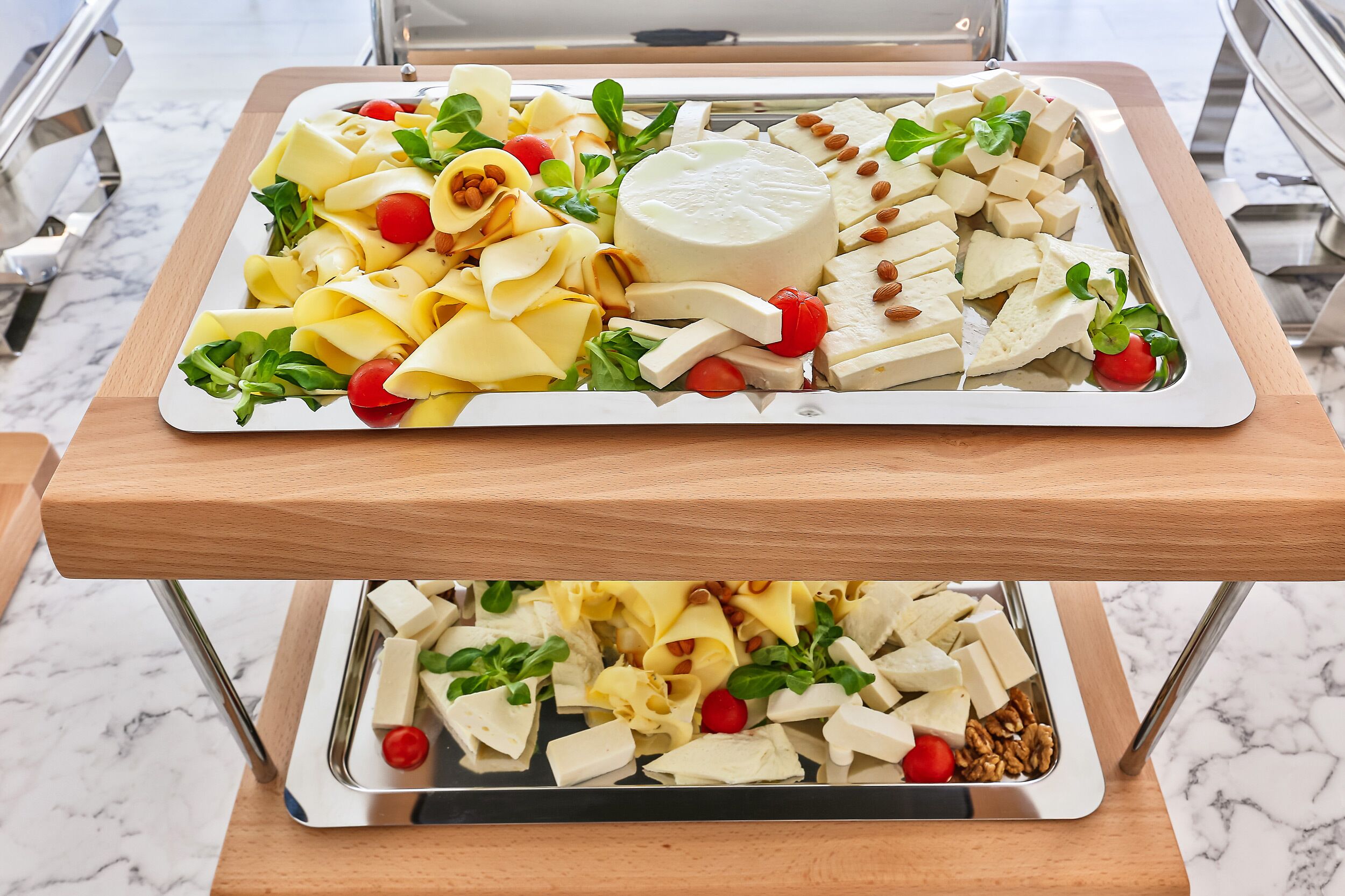 Una bandeja con varios tipos de queso, nueces y verduras sobre una mesa de madera.
