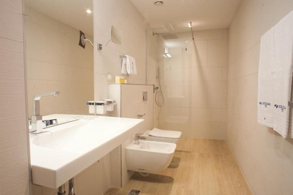 Un baño moderno con un lavamanos blanco, dos inodoros y una zona de ducha.